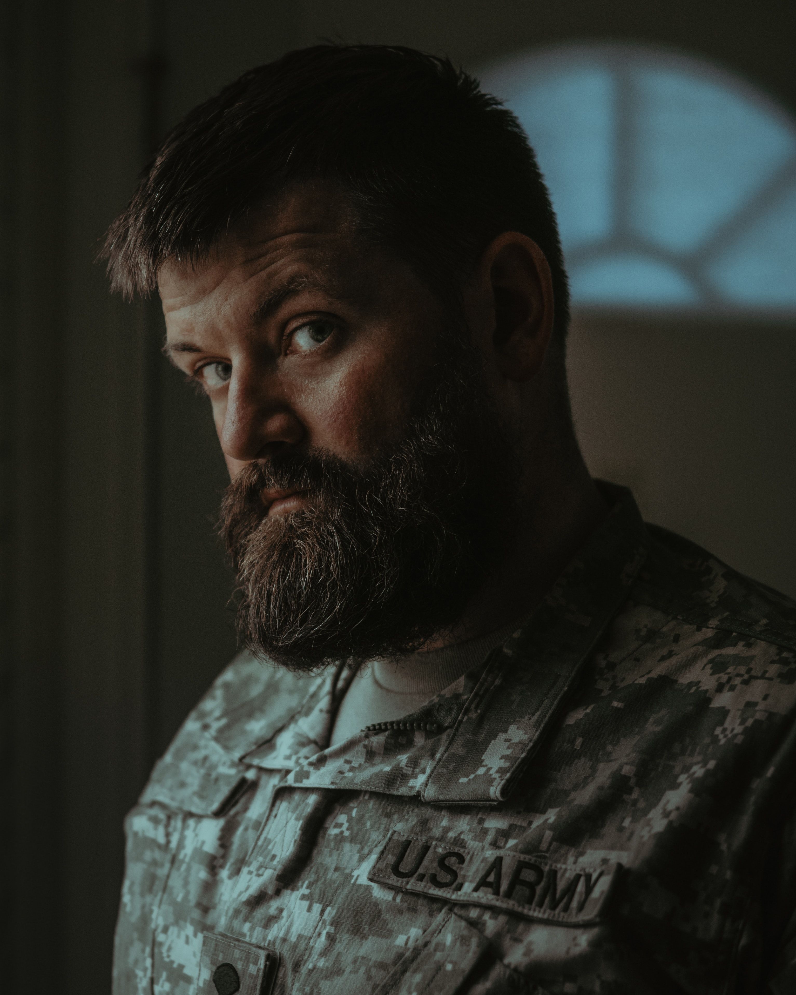 A contemplative male veteran with a beard wearing a US Army uniform indoors in Portland, Oregon.