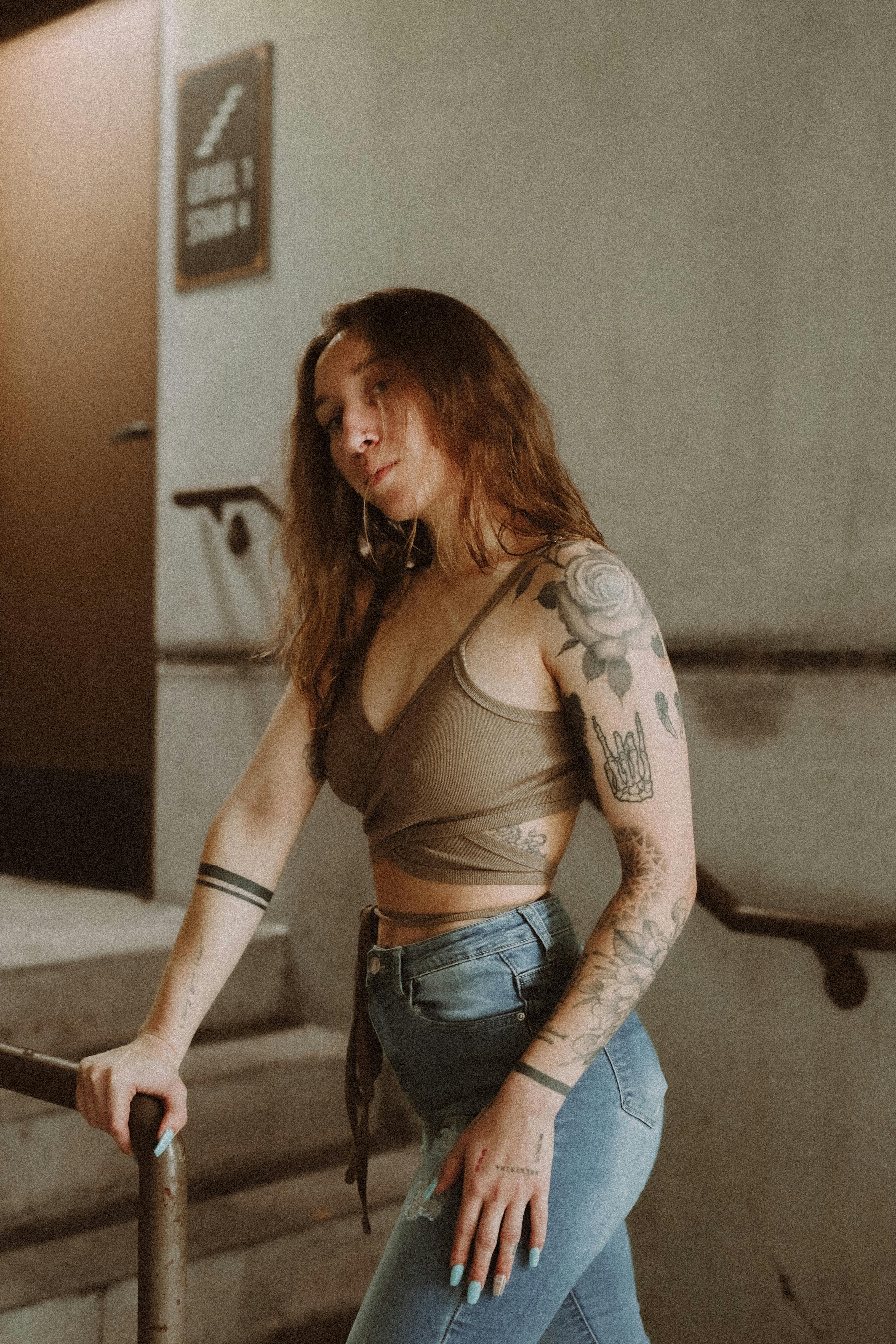 A woman with tattoos poses on a staircase indoors, showcasing her fashion style.