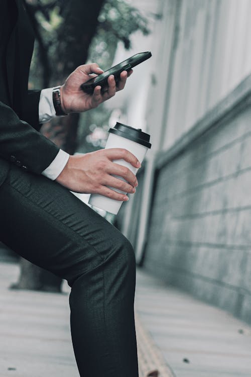 Close-up of a Man in a Suit Holding a Coffee Cup and a Smartphone 