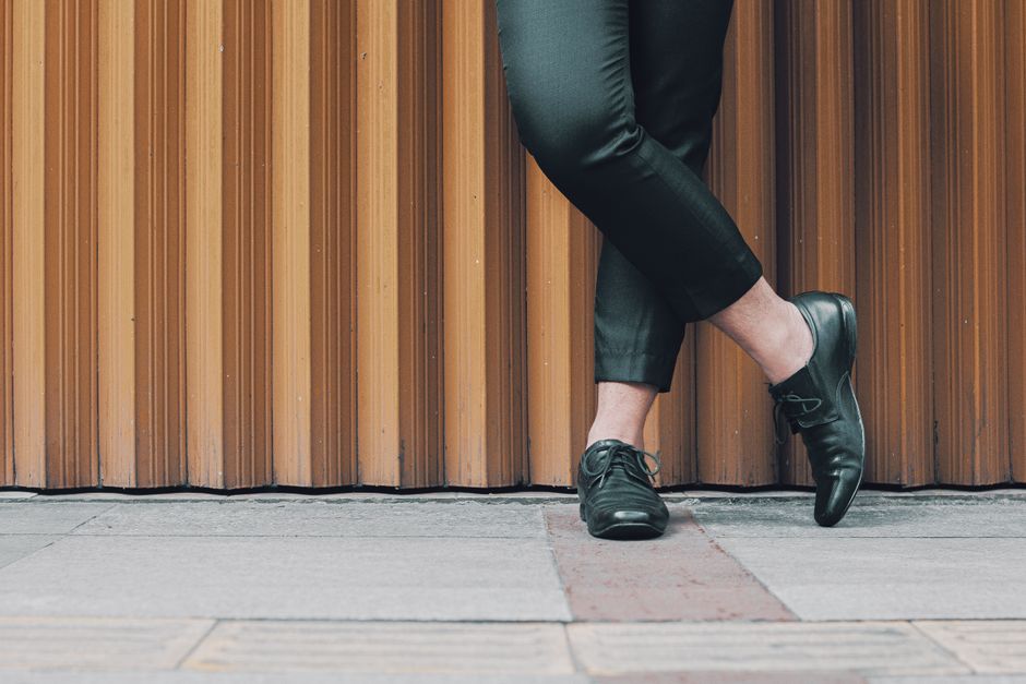 A fashionable man in black pants and leather shoes stands against a textured background. A fashionable man in black pants and leather shoes stands against a textured background.