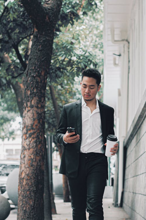 Man in a Suit Walking with a Smartphone and a Coffee in his Hands 