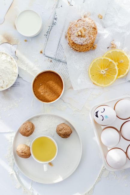 A top view of baking essentials with lemon slices, eggs, and a cup of juice on a white background.