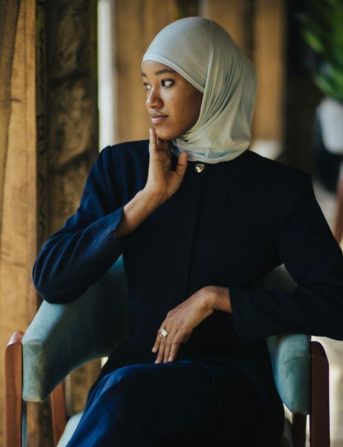 Free A sophisticated woman in a hijab sits gracefully on a chair indoors with natural light. Stock Photo