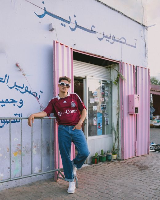 Young man in stylish outfit poses against a vibrant pink storefront in Casablanca, Morocco.