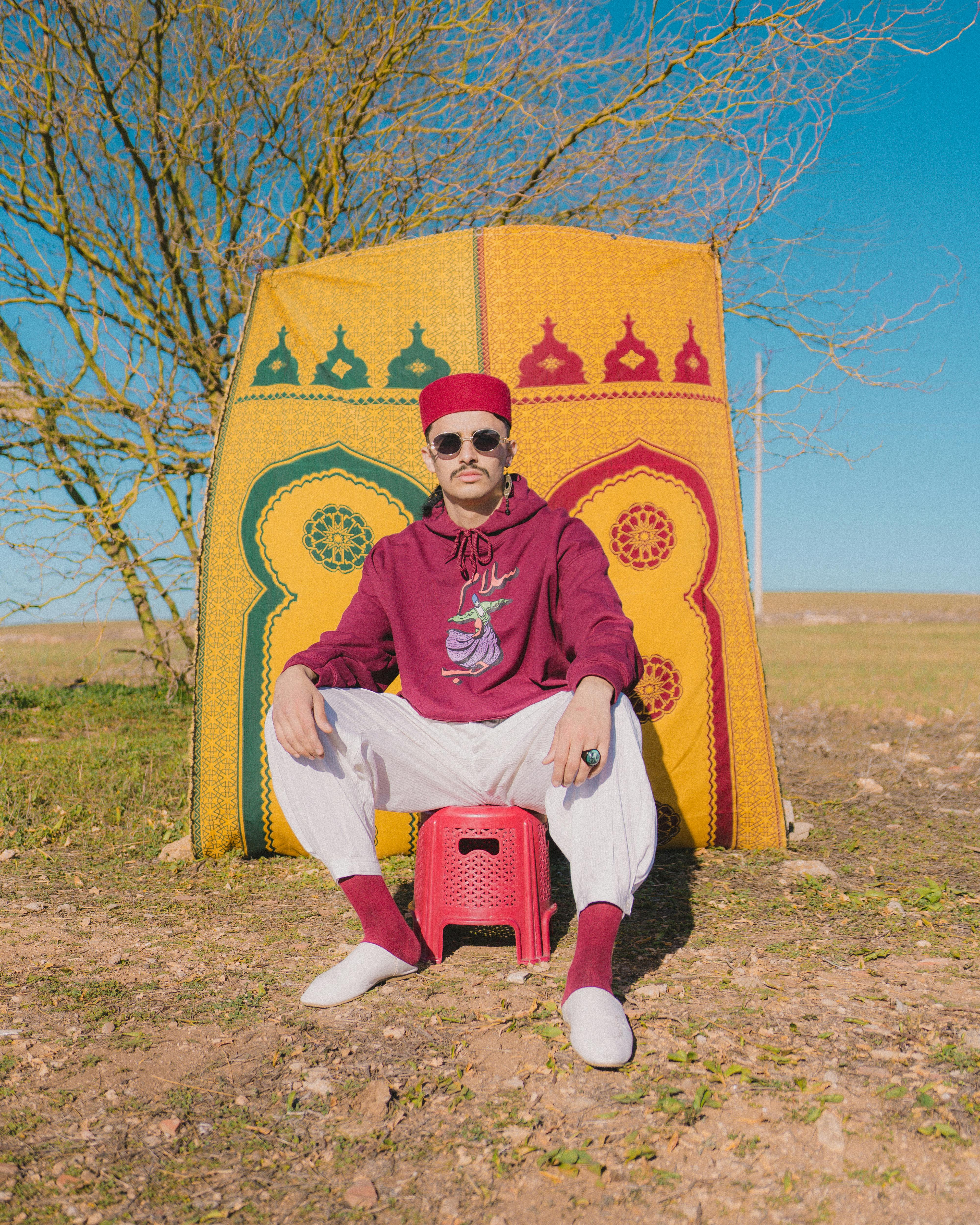 Stylish man in Moroccan attire sitting outdoors, showcasing a blend of tradition and modern fashion.