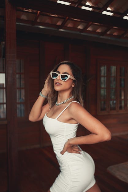 Portrait of smiling young woman wearing sunglasses, white vest and flip  flops. Stock Photo by Mint_Images
