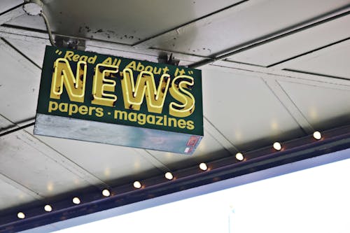 Free From below of illuminated signboard with news papers magazines inscriptions hanging on metal ceiling on street Stock Photo
