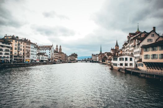 Scenic view of Zurich's historic buildings along the Limmat River under a cloudy sky.