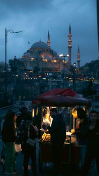 Dusk view of Istanbul street life with a food cart and illuminated mosque in the background.