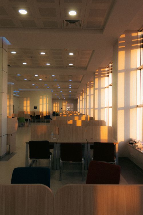 Free A spacious sunlit conference hall with rows of tables and chairs, creating a warm atmosphere. Stock Photo