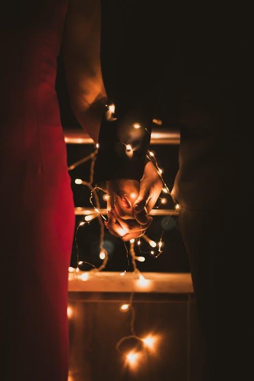 Close-up of a Couple Holding Hands Tied with Christmas Lights 