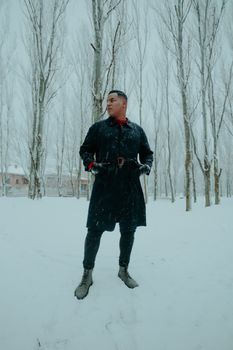Man in a black coat posing in a snowy winter park setting.