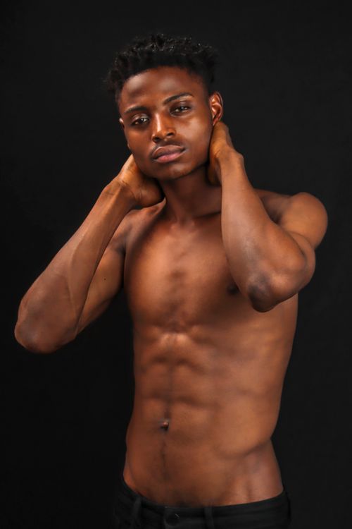 Free Topless portrait of a young male model posing against a black background with hands on neck. Stock Photo