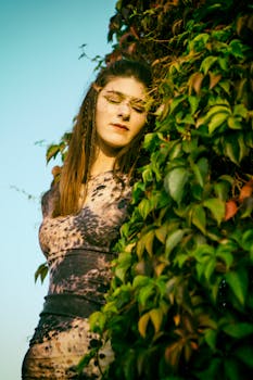 A woman in a patterned dress poses outdoors amidst lush green foliage, exuding style and grace.