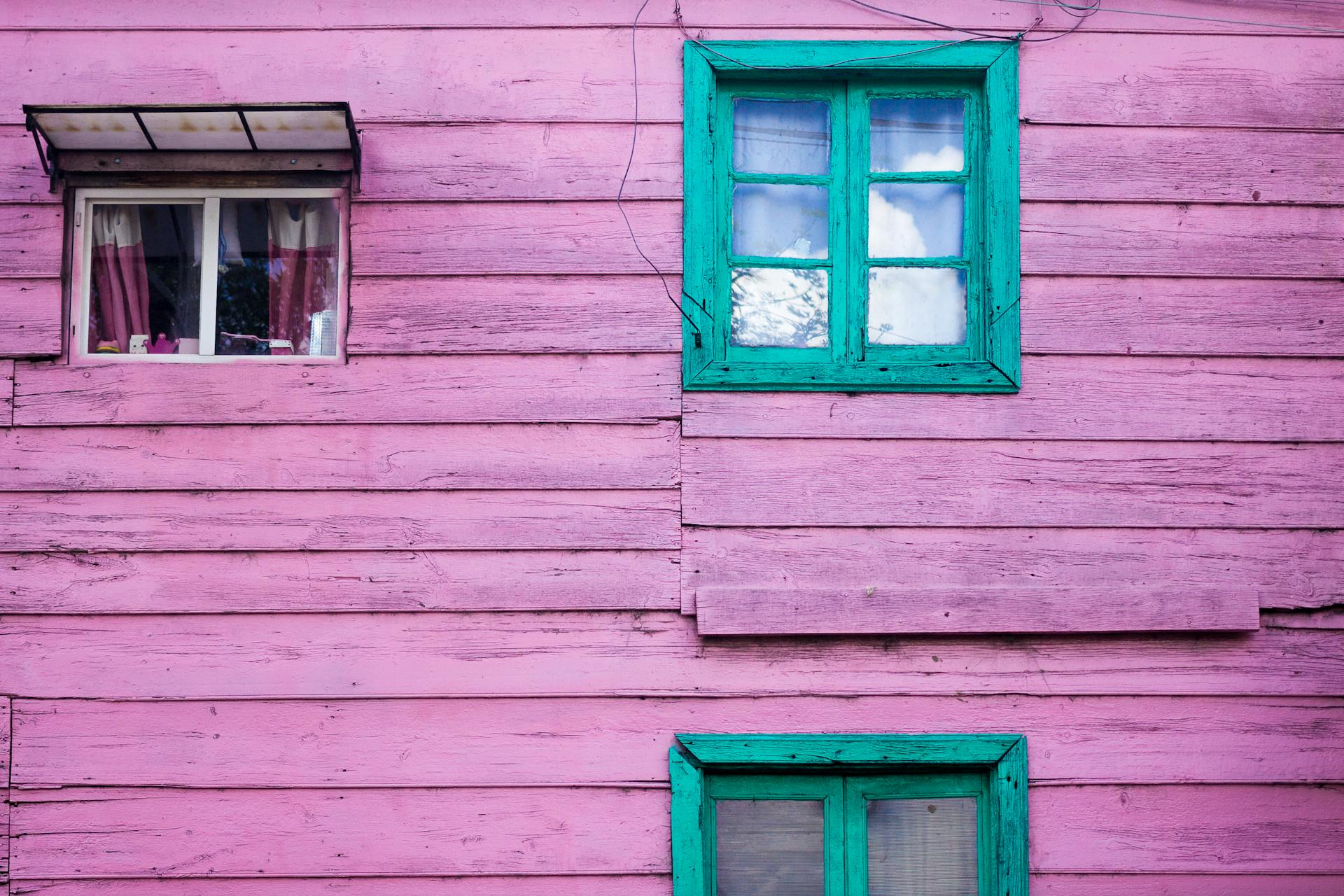 A colorful wooden house exterior with pink walls and vibrant green windows, creating a bold contrast.