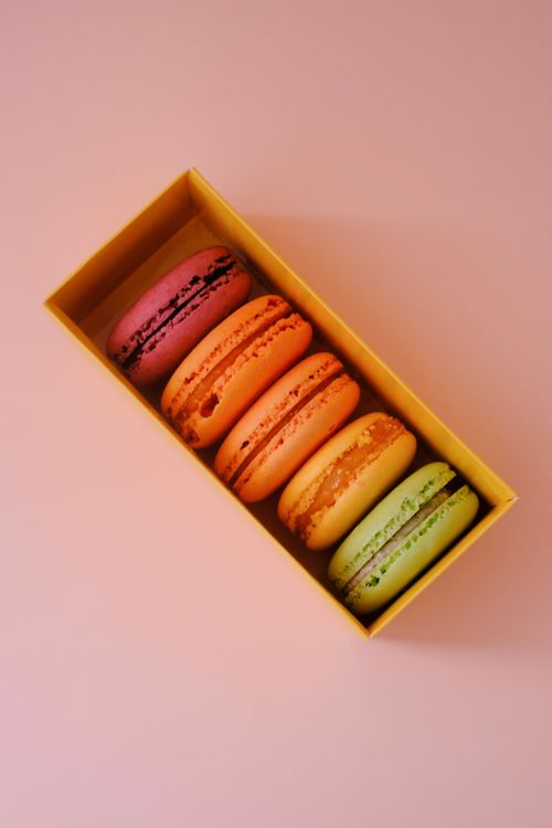 Free A vibrant collection of assorted macarons displayed in a box, placed on a pastel pink background. Stock Photo