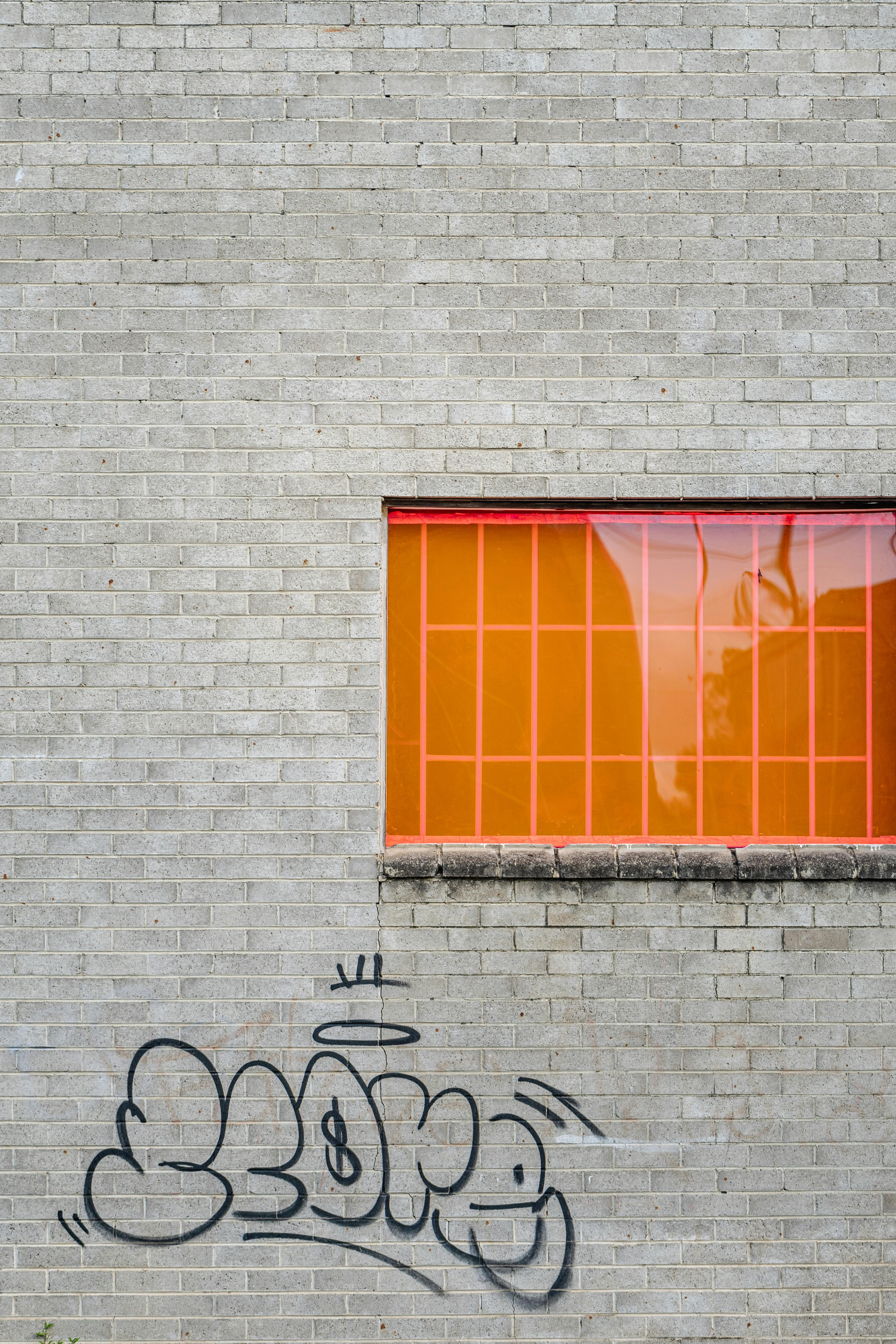Vibrant urban scene featuring graffiti on a brick wall with a striking orange window.