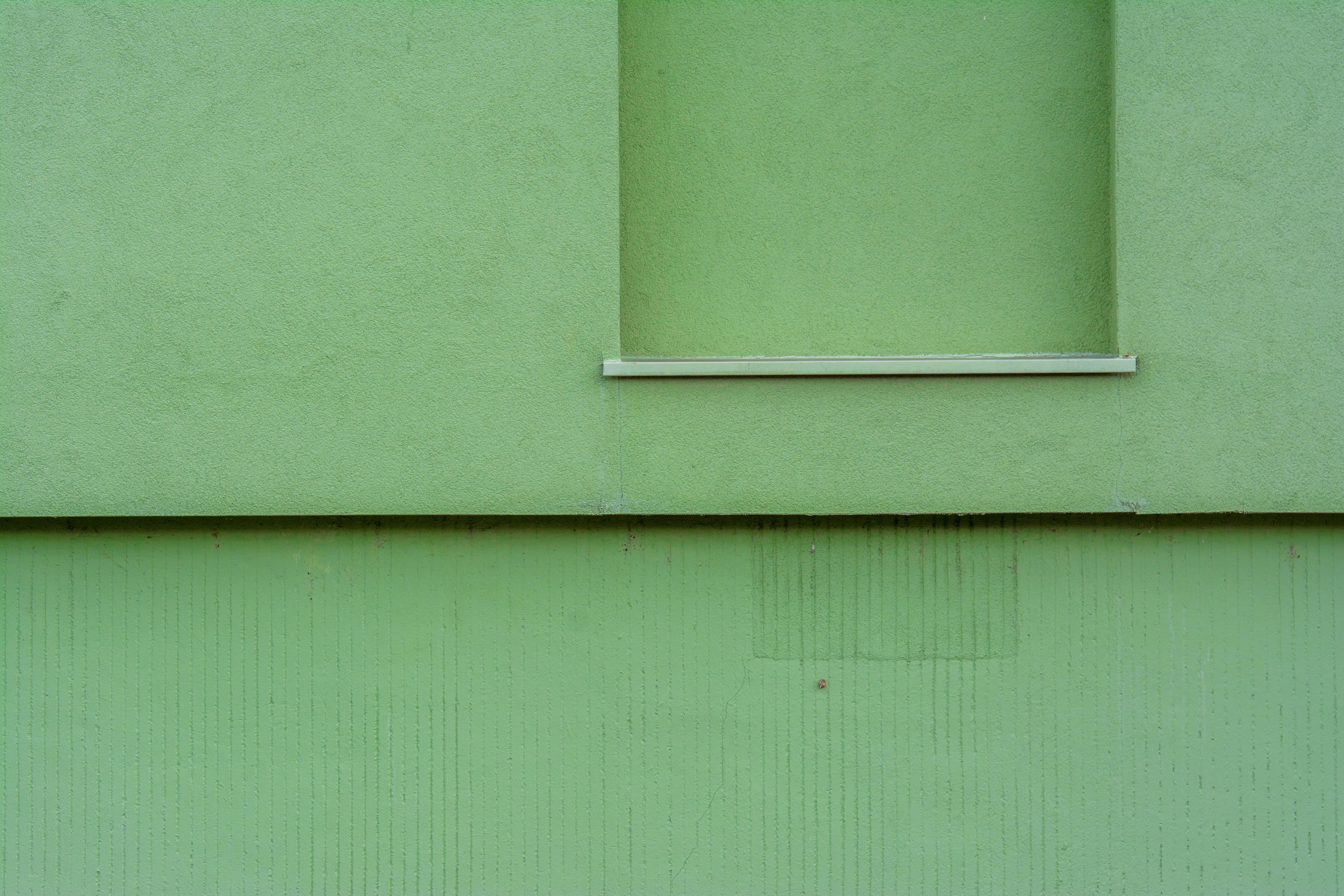 A green building facade with a minimalist design and a window shelf.