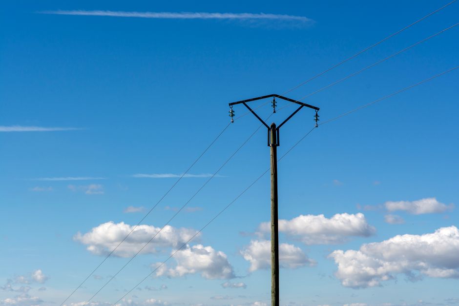 Lone utility pole under a bright blue sky with clouds, symbolizing electrical power.