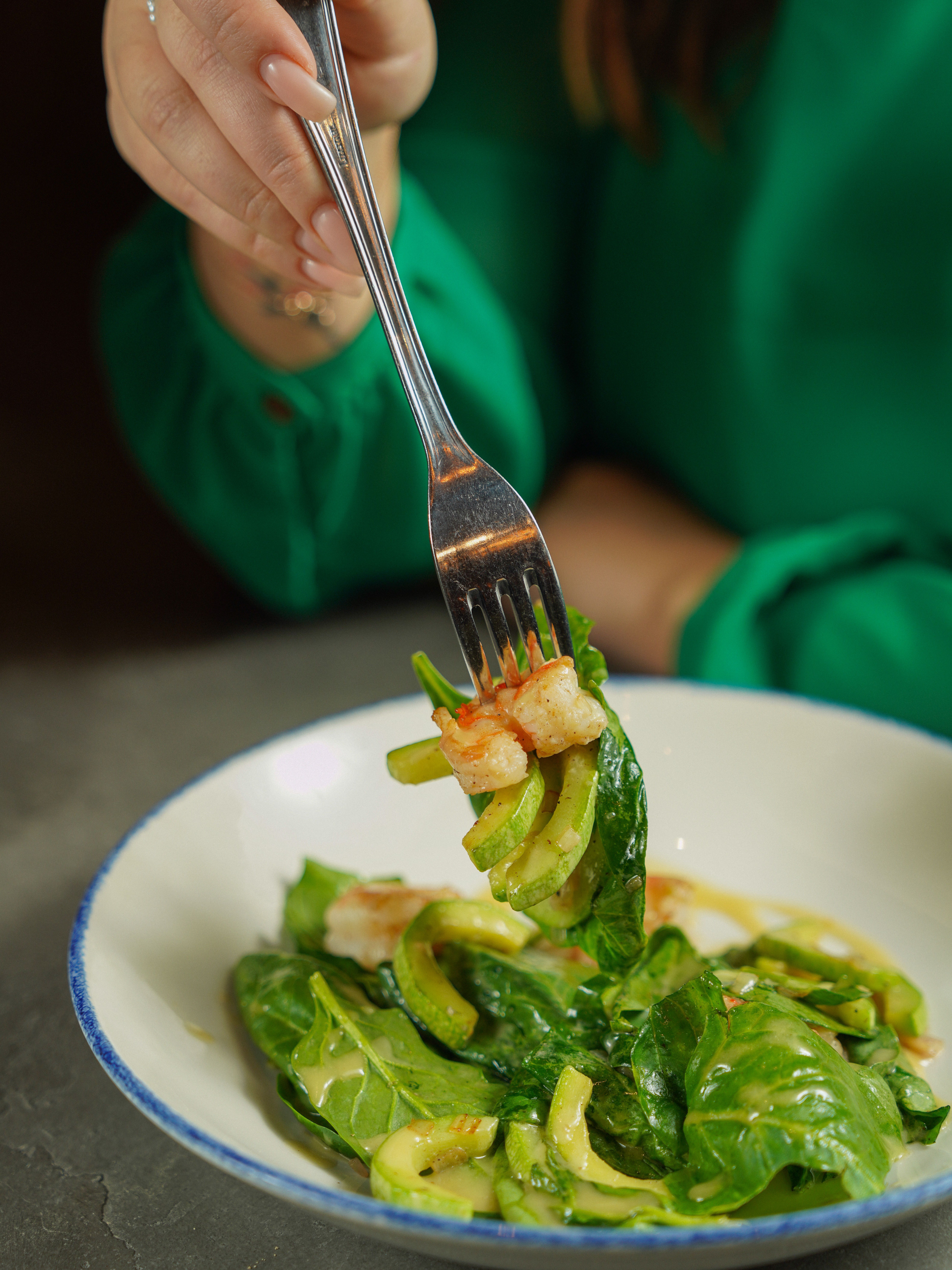 Close-up of a spinach salad with avocado and shrimp on a fork.