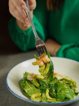Close-up of a spinach salad with avocado and shrimp on a fork.