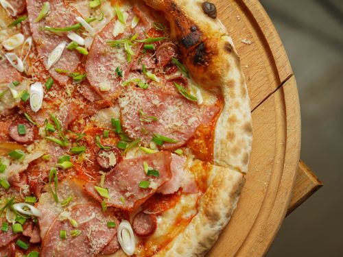 Free Close-up of a delicious Italian pizza topped with ham, cheese, and fresh greens on a wooden platter. Stock Photo