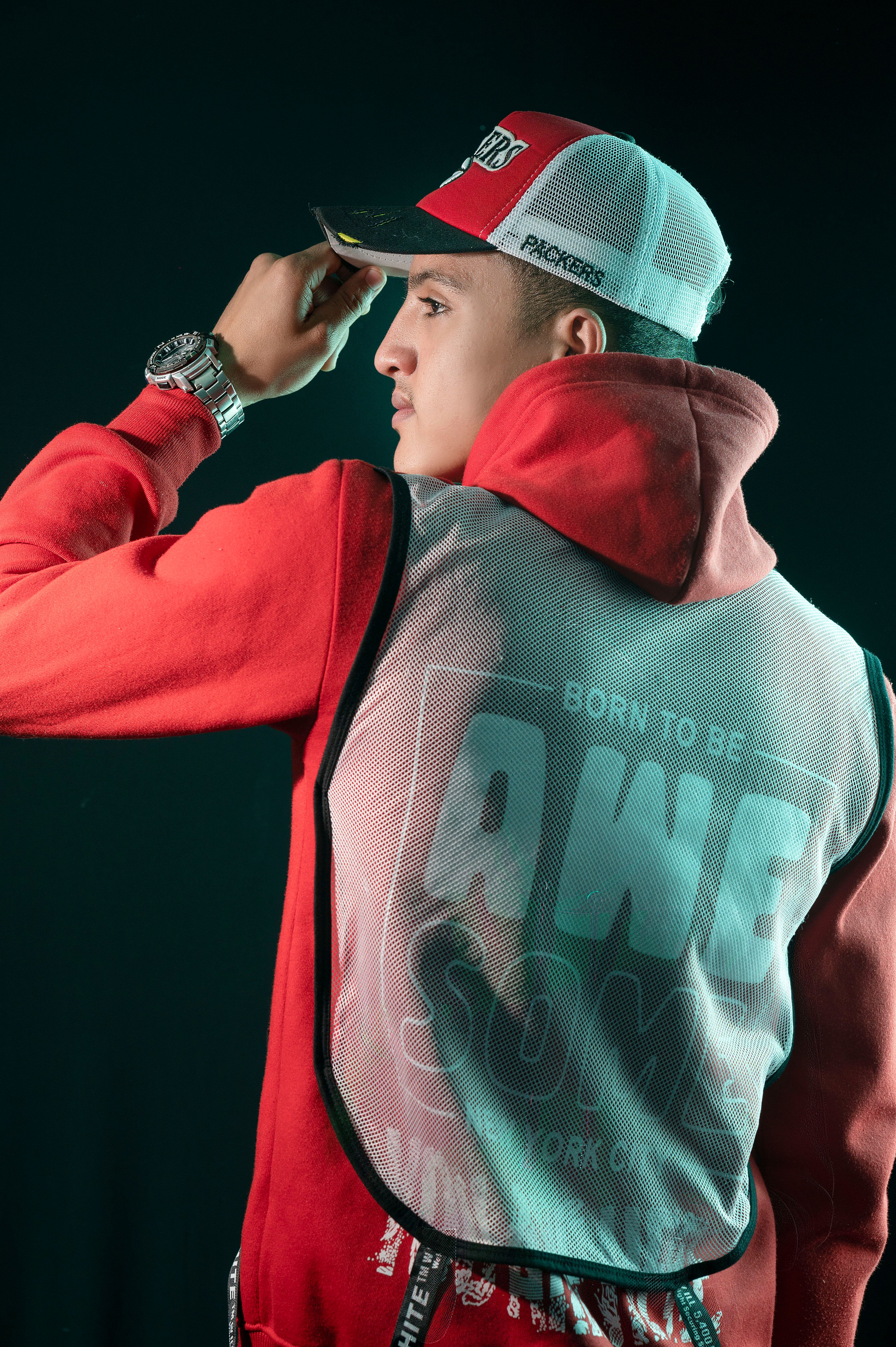 Young man in a red hoodie and cap posing confidently in a studio setting, showcasing modern sportswear fashion.