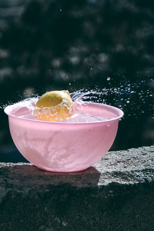 Free A vibrant lemon splashing in a pink bowl of water under sunlight, capturing motion and freshness. Stock Photo