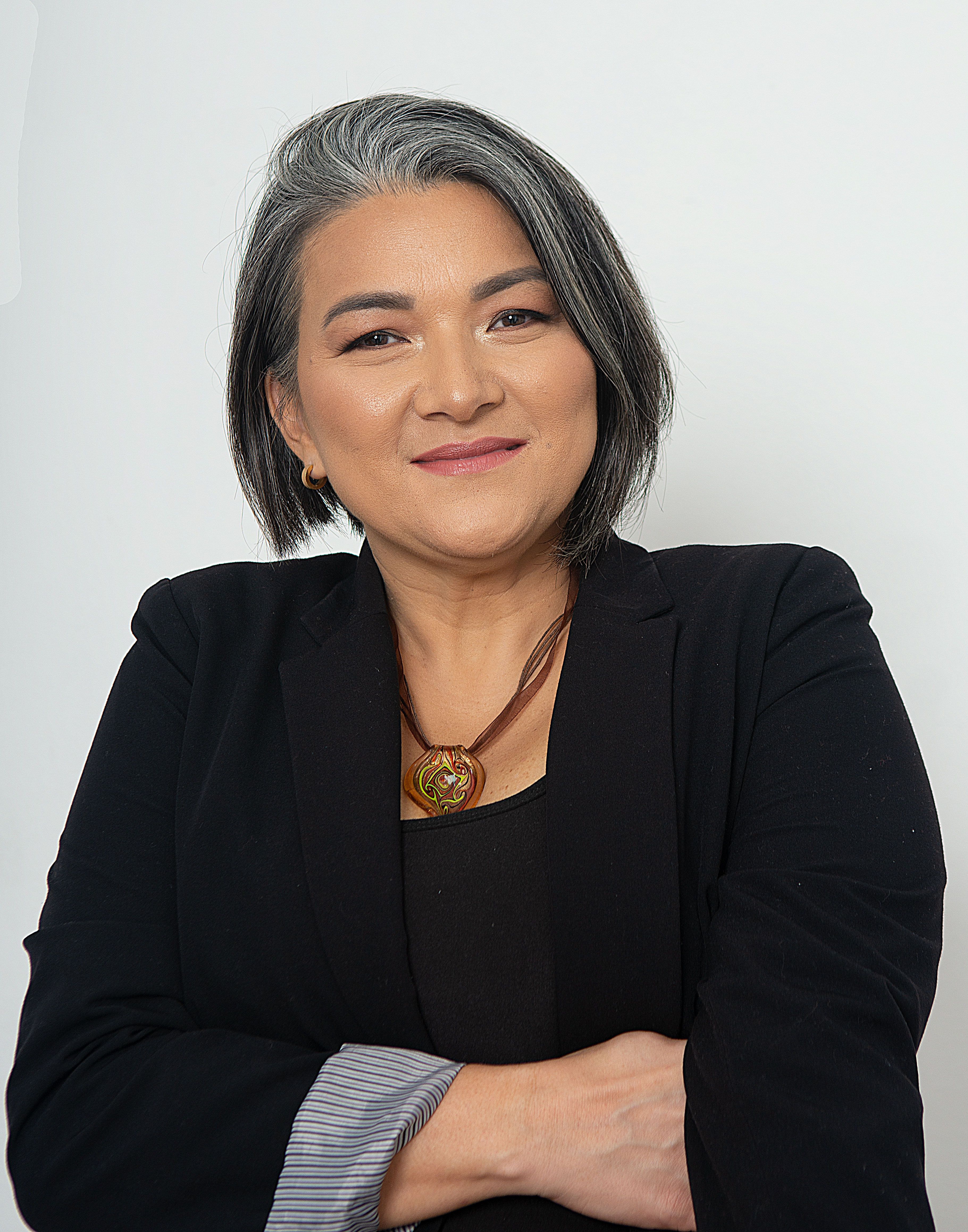 Portrait of a senior woman with gray hair in a black suit posing with arms crossed.