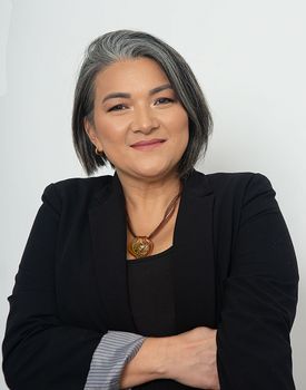 Portrait of a senior woman with gray hair in a black suit posing with arms crossed.