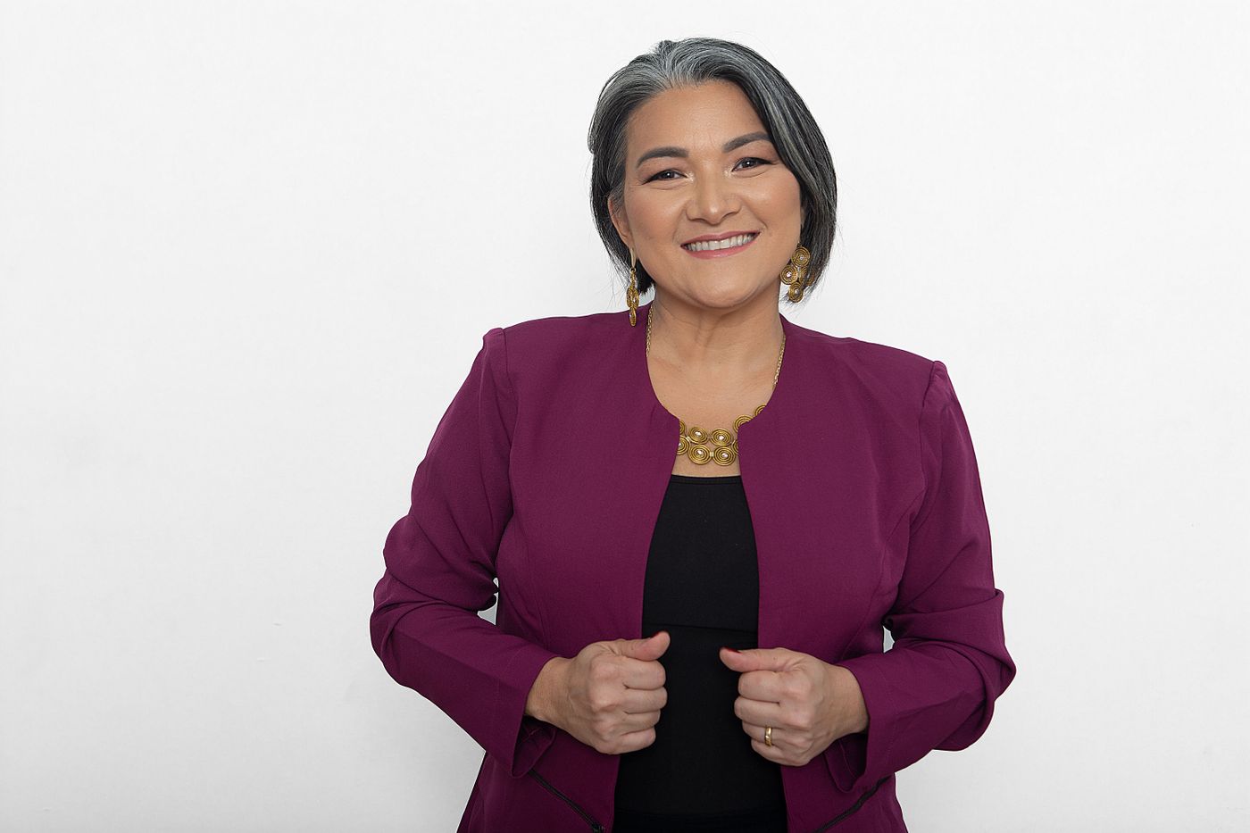 Confident woman with gray hair, wearing a purple blazer and smiling warmly