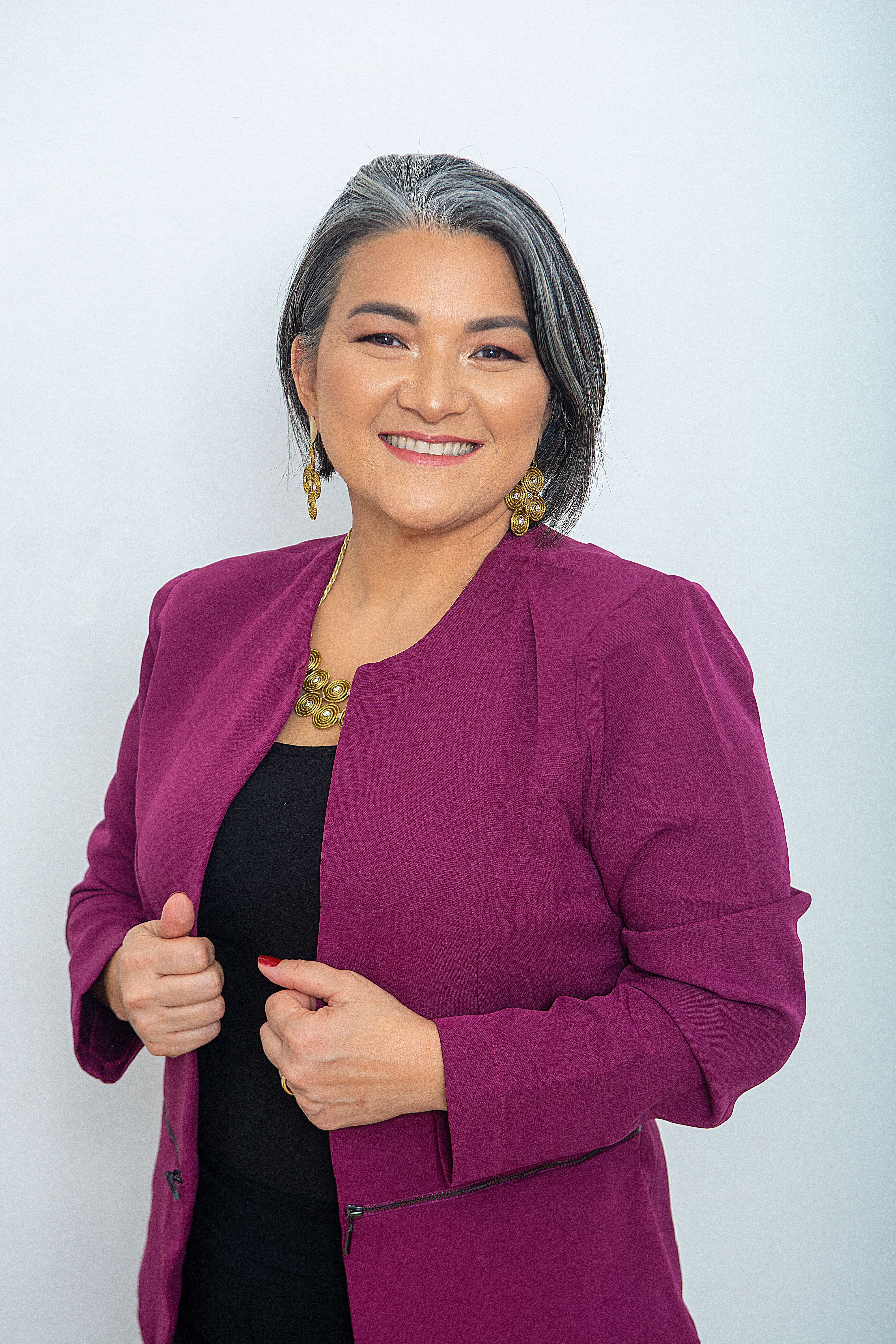 A smiling woman with gray hair posing confidently in a purple blazer against a white background.