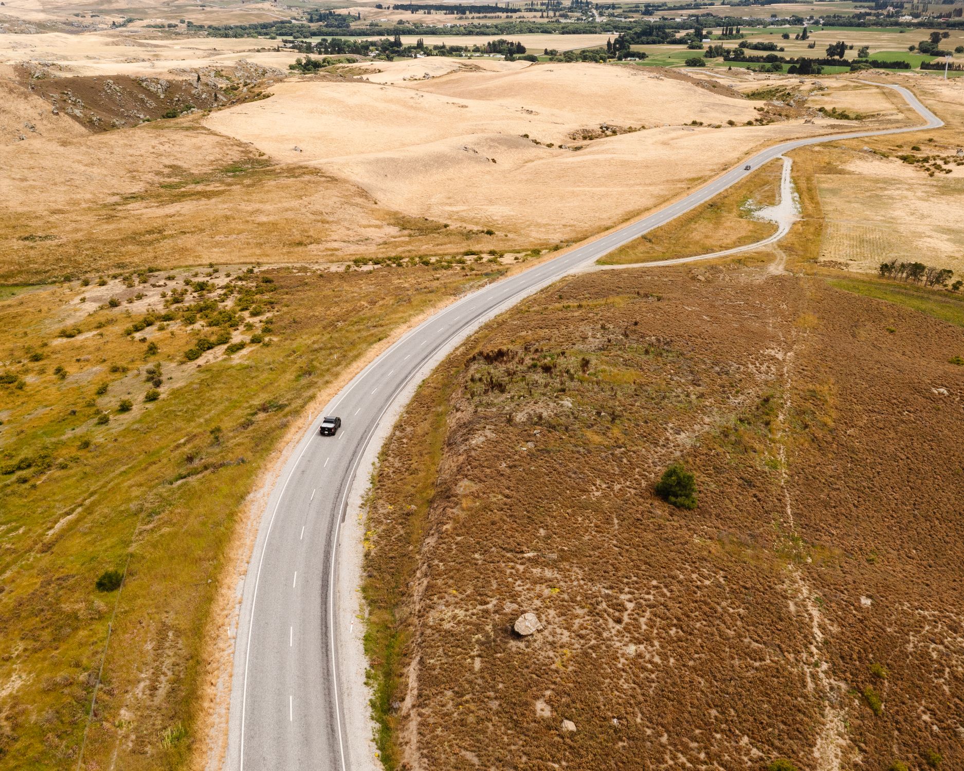 Drone view of a winding road through the golden landscapes of Otago, New Zealand.