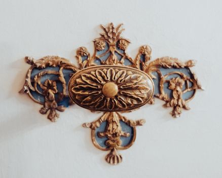 A close-up of an intricately designed brass ornament on a white wall, showcasing classic elegance.