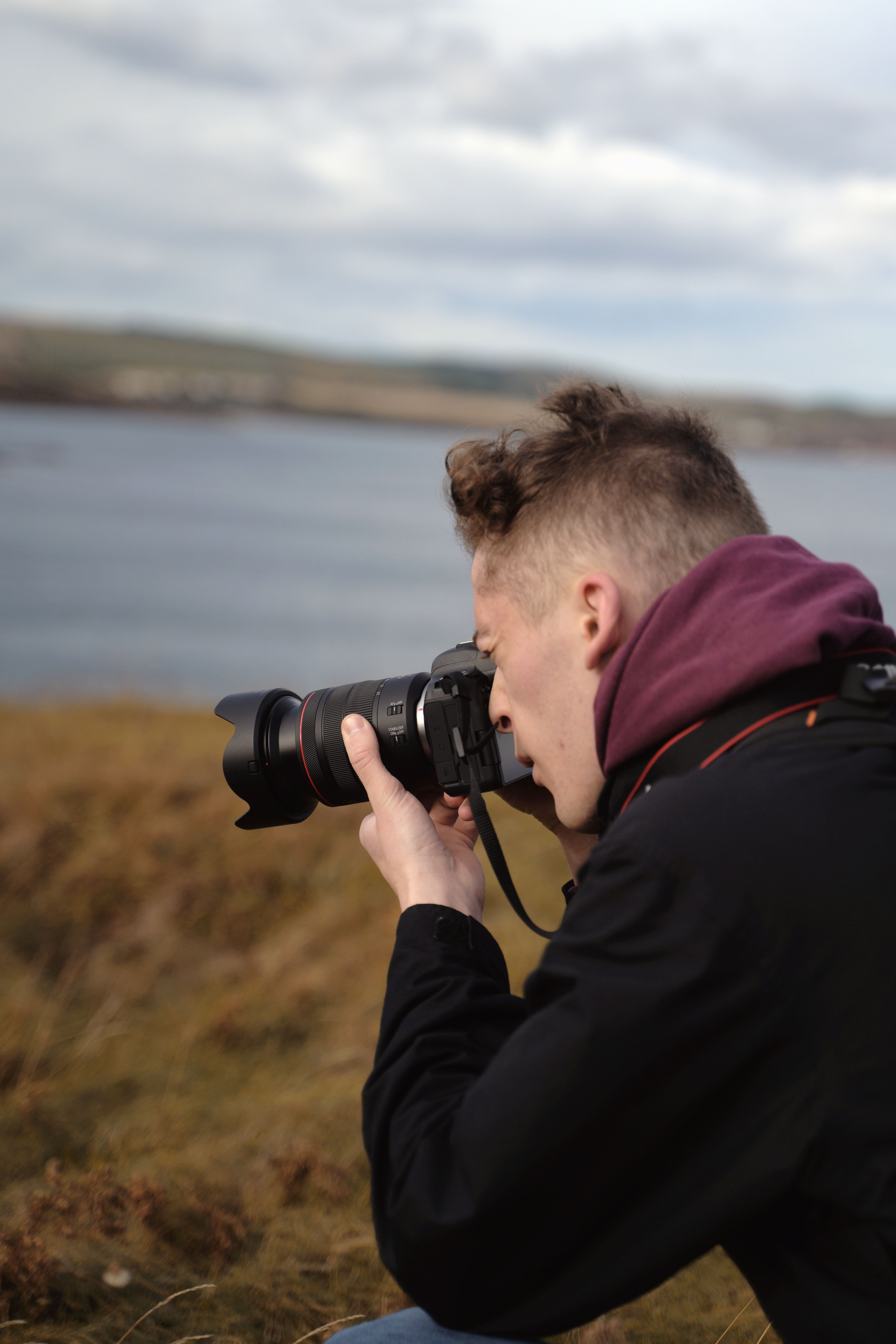Male photographer taking landscape photos by a lake on a cloudy day.