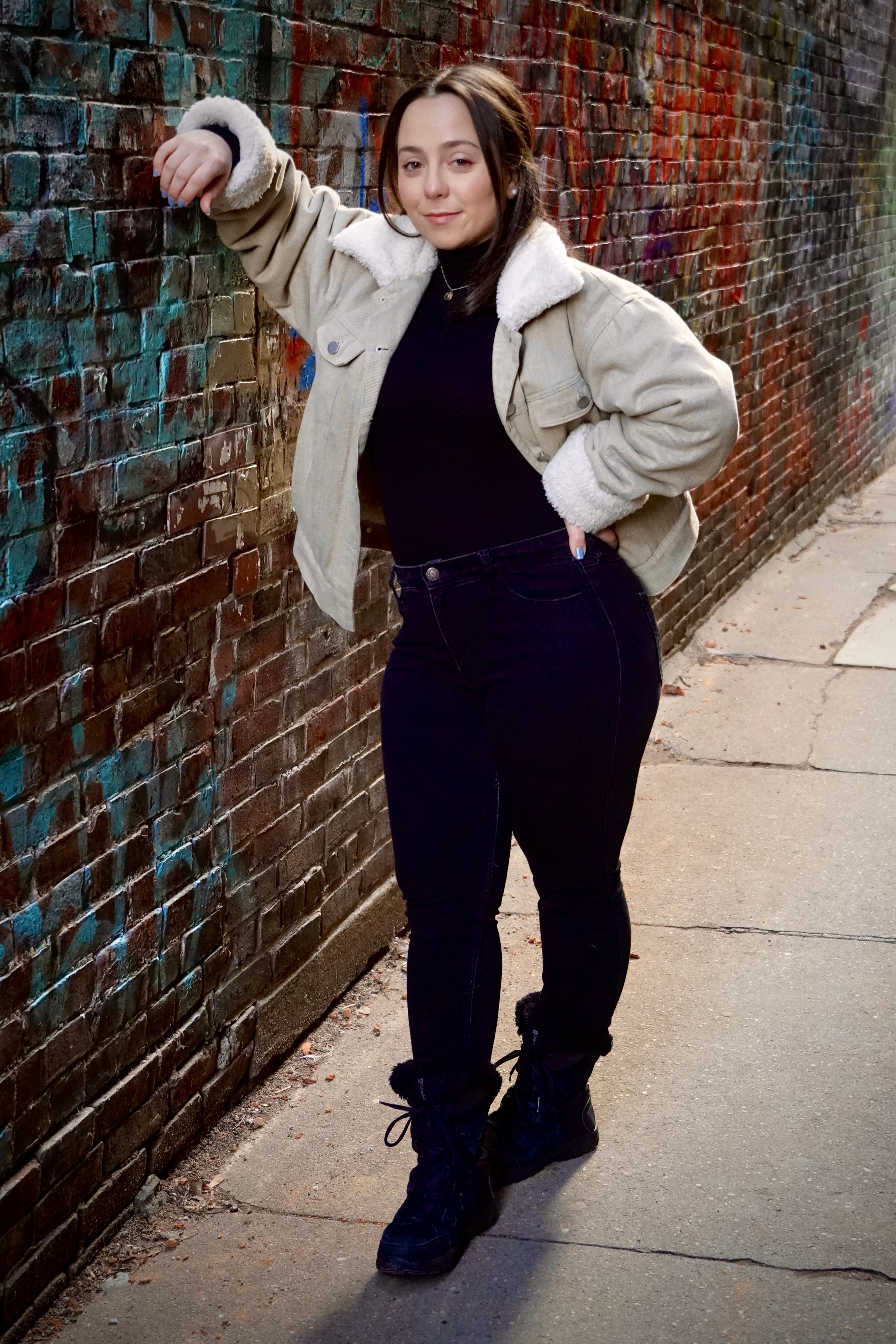Woman in casual wear posing against graffiti wall in Portland alley.