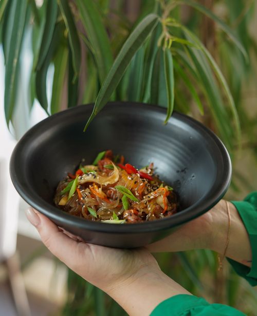 Free Close-up of a delicious Asian rice noodle dish in a black bowl held by a woman. Stock Photo