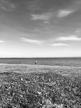 A lone person stands at the edge of a monochrome oceanfront, capturing solitude and vastness.