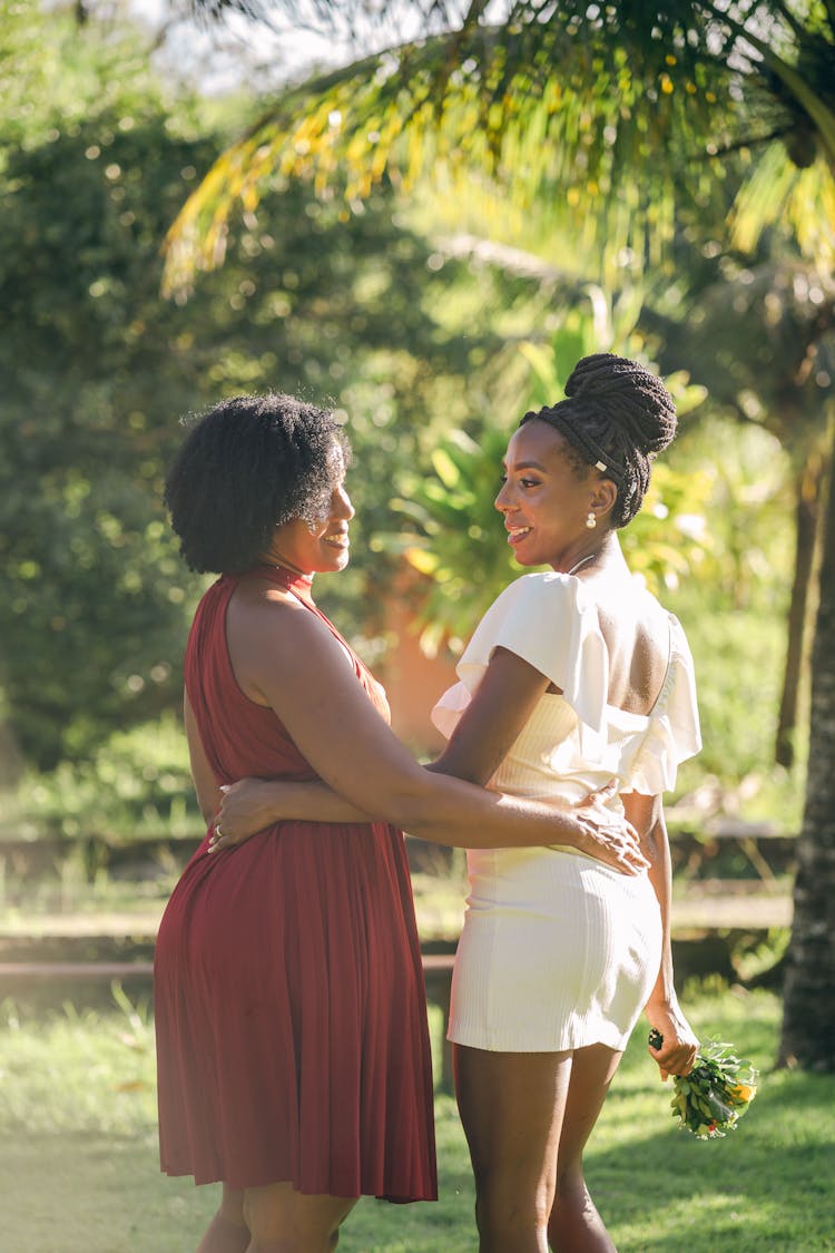 Bride And Bridesmaid Holding Arms Around Each Other And Smiling 