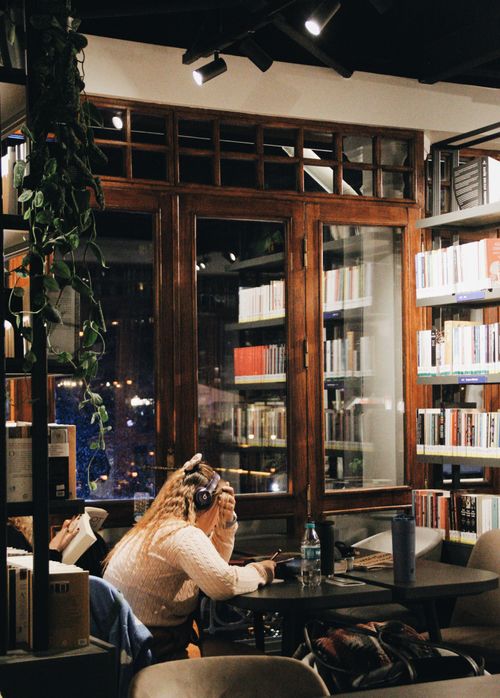 Free A woman enjoys reading with headphones in a cozy Istanbul bookstore cafe at night. Stock Photo