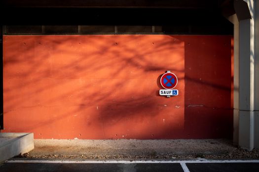Parking sign on a vibrant orange wall in urban setting, with shadows.