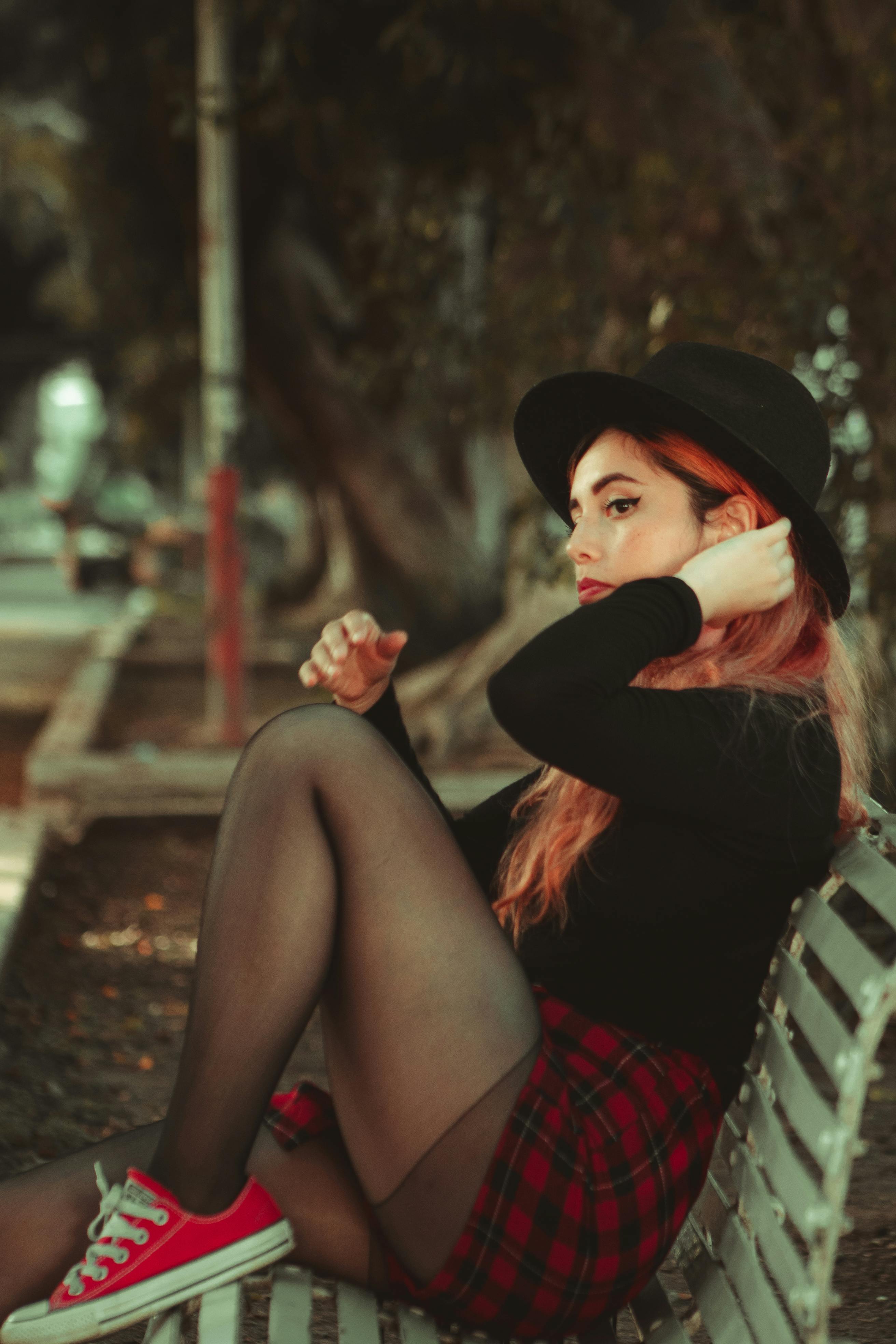 一位戴着黑色帽子、穿着格子裙的优雅女子在户外长凳上摆着姿势