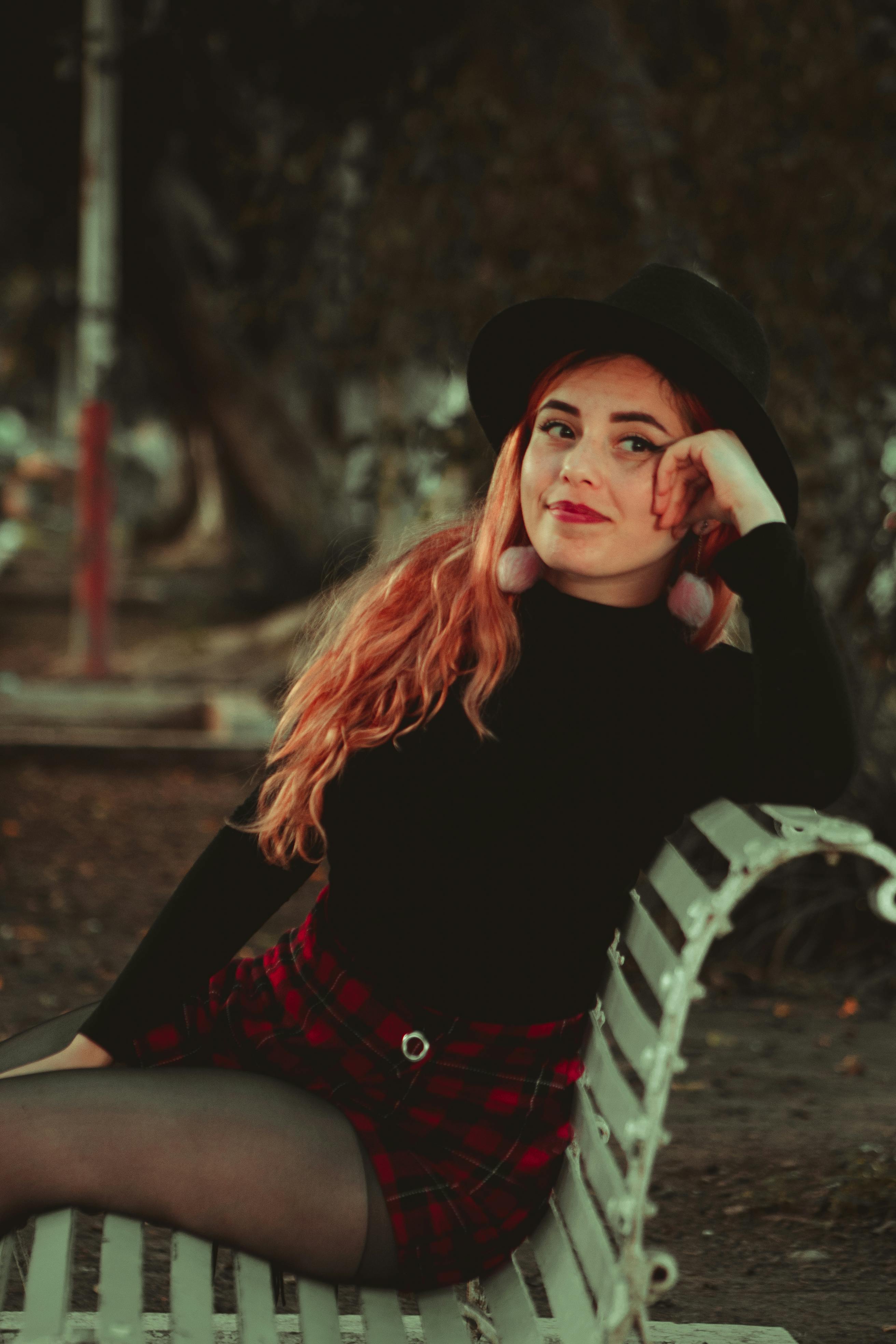 一位戴着软毡帽、穿着格子裙的时尚女士，自信地坐在公园长凳上