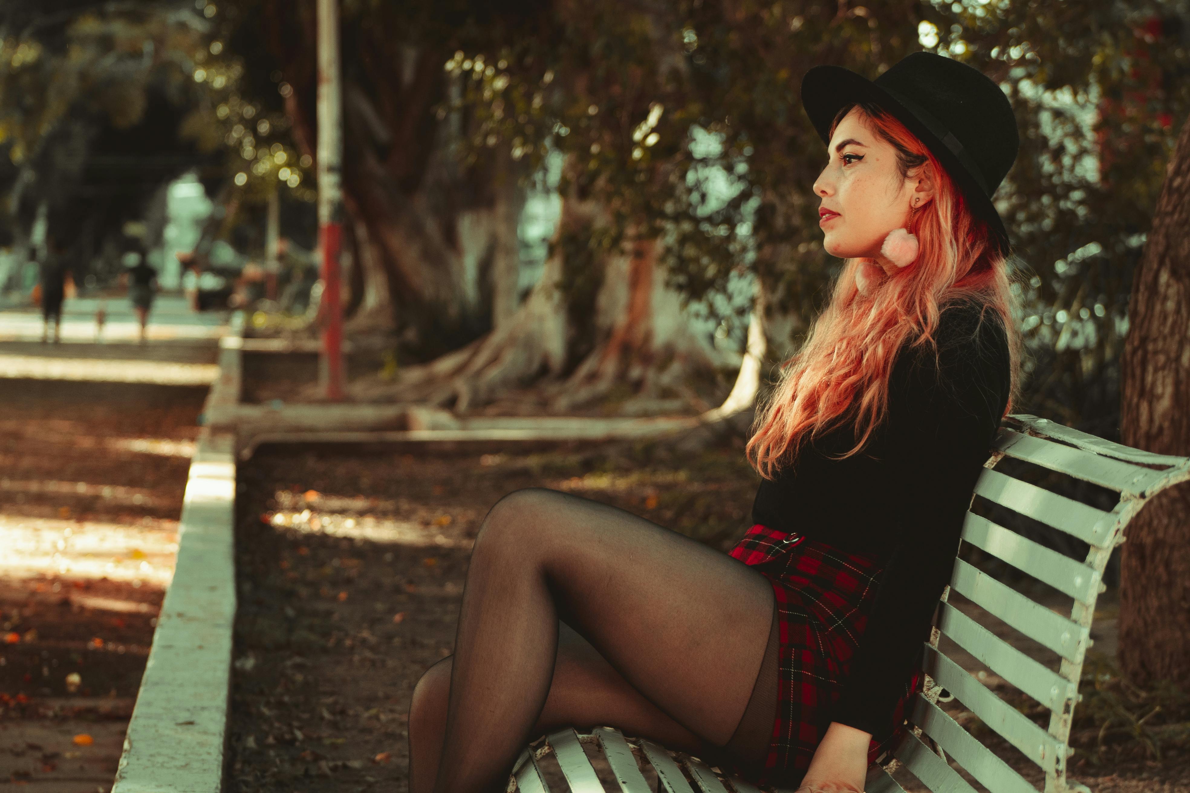 一位年轻女子，头发鲜艳，优雅地坐在公园长凳上，融入城市环境