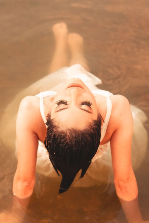 Free A woman in a white dress relaxes in water, captured from above for a peaceful fashion scene. Stock Photo