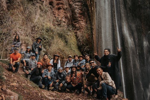 A diverse group of friends gathered by a majestic waterfall in Ollantaytambo, Cuzco, Peru, on a vibrant day.