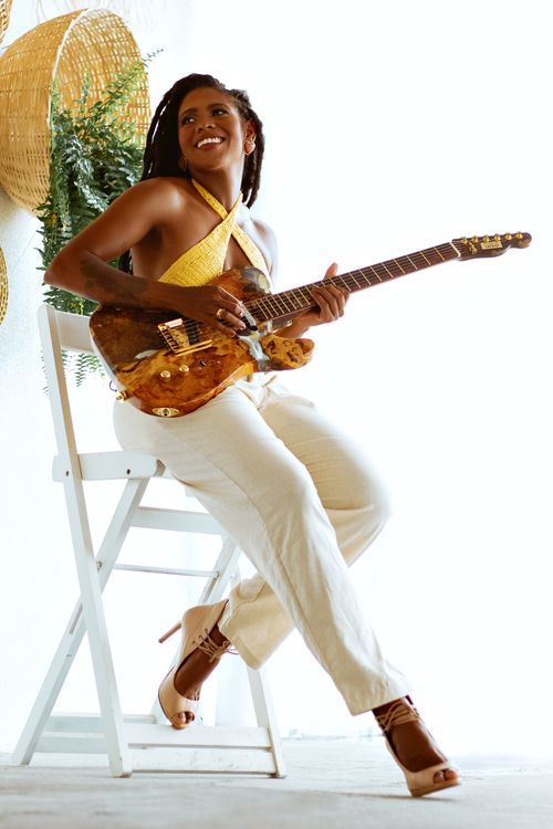 Free Chic woman in yellow top and high heels playing guitar in bright studio setting. Stock Photo
