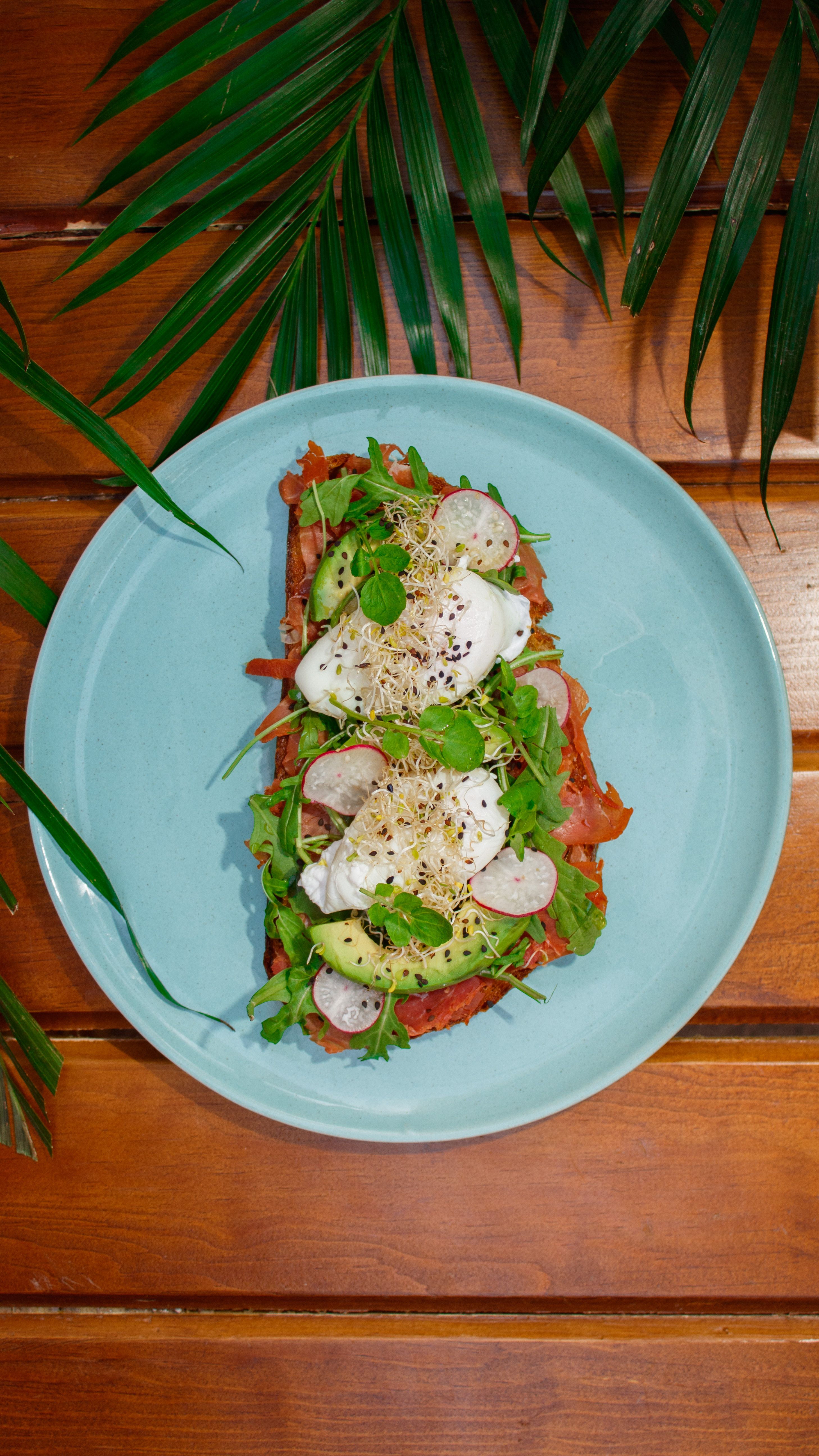 Delicious open-faced sandwich with fresh avocado, radish, and greens on a wooden table.