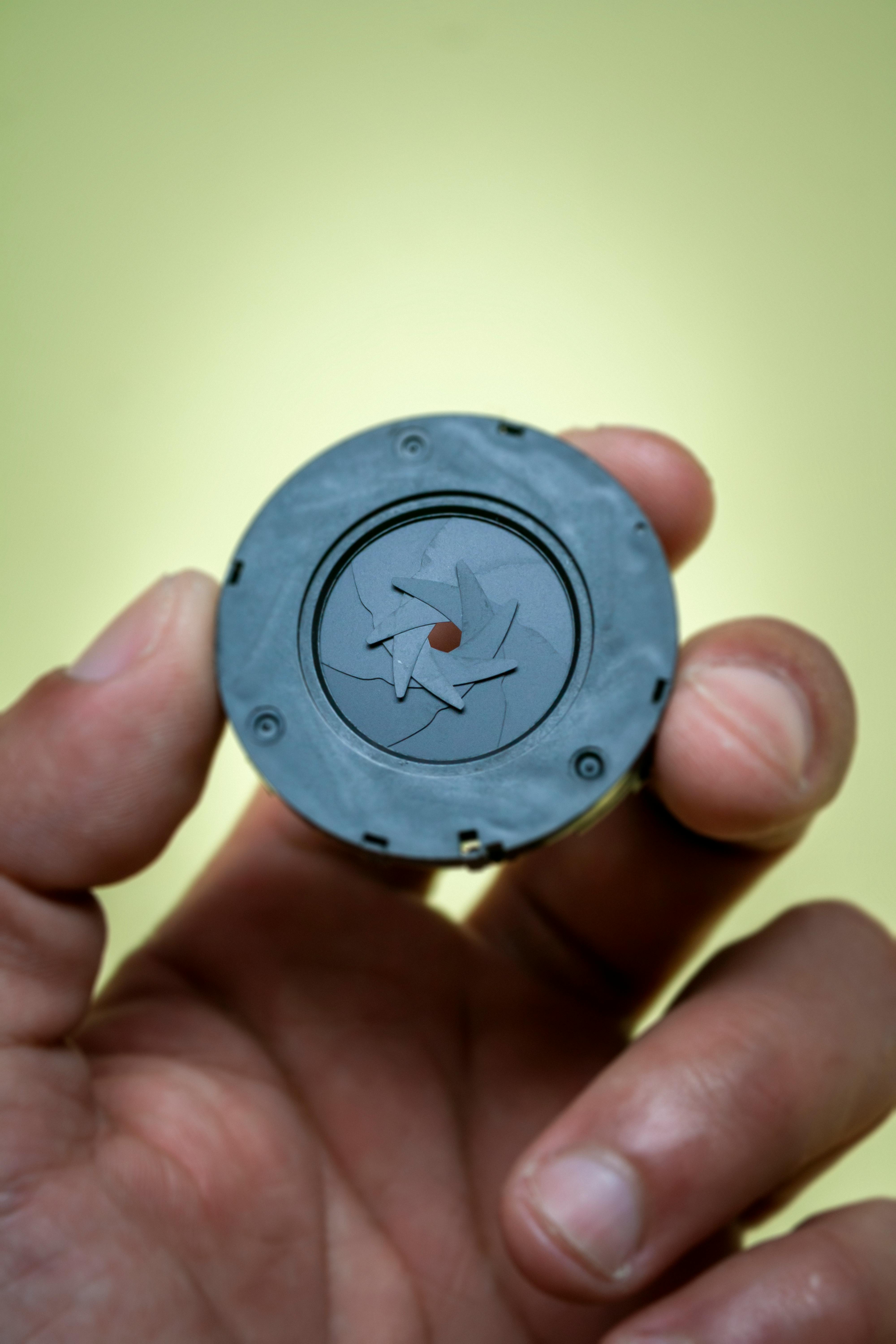Macro shot of a camera aperture held by a hand against a green background.