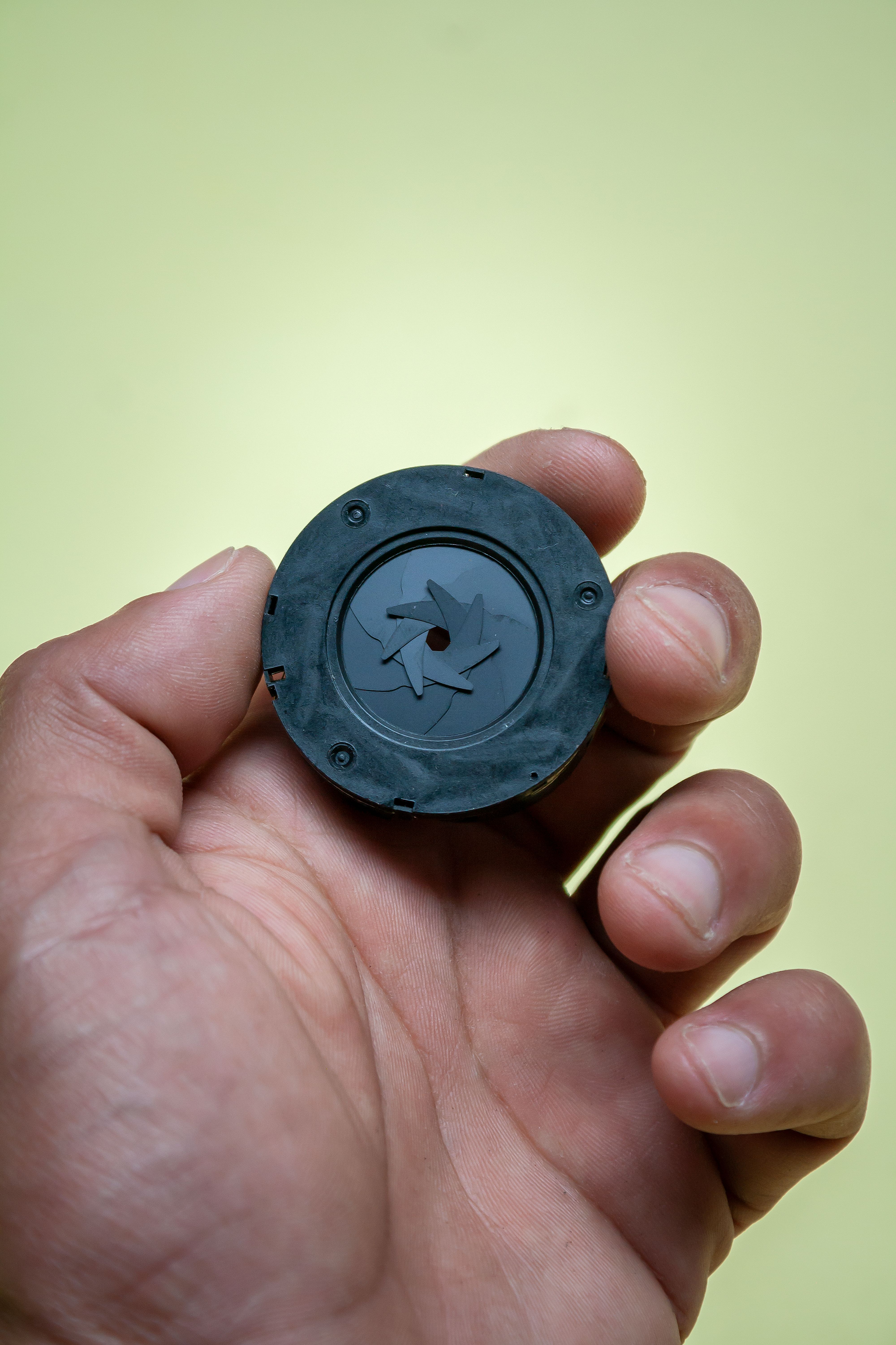 Detailed view of a hand holding a camera lens aperture mechanism against a green background.